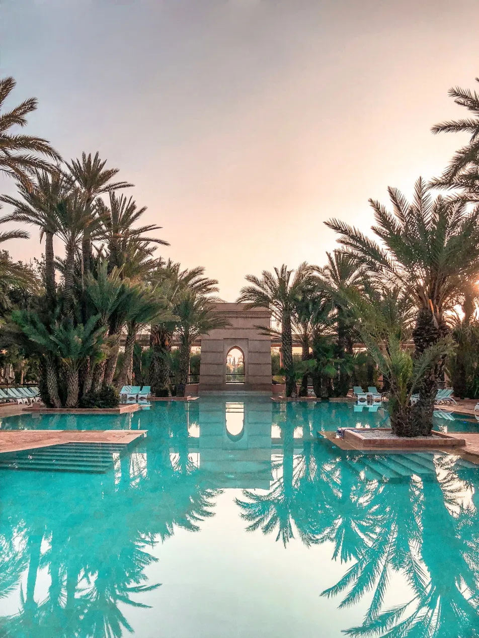 Turquoise pool with Moroccan stone archway and date palms